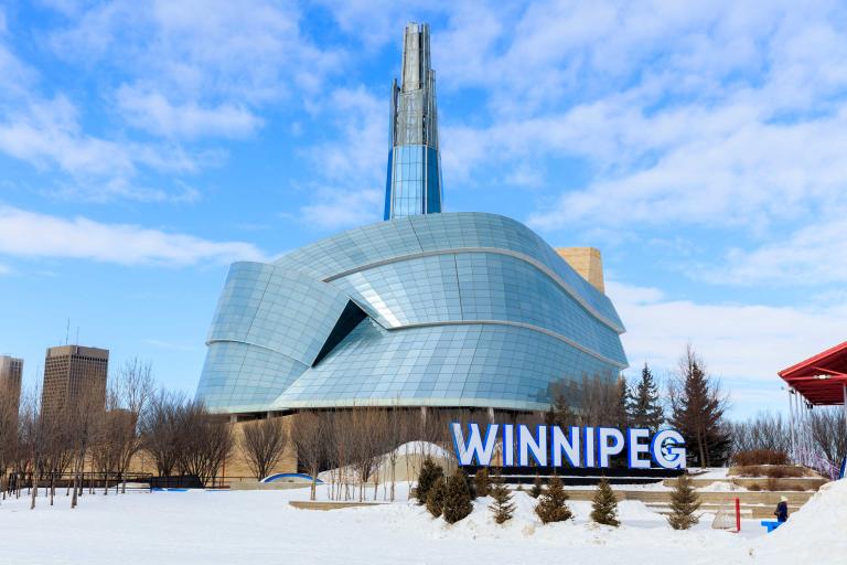 Image of the CMHR in the winter with Winnipeg sign. Partially obscured.