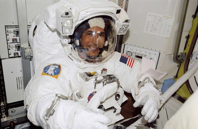 A smiling man in an astronaut suit. Partially obscured.