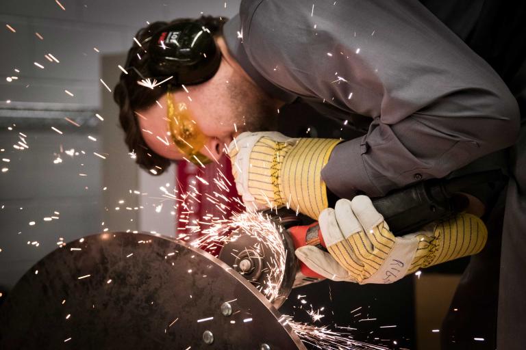 Close-up of a person in coveralls sending sparks flying while grinding metal.