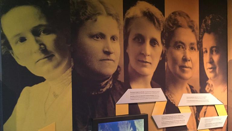 Large photographs of five women on the wall of a Museum exhibit. They are the "Famous Five" - Nellie McLung, Emily Murphy, Irene Parlby, Louise McKinney and Henrietta Edwards. Partially obscured.
