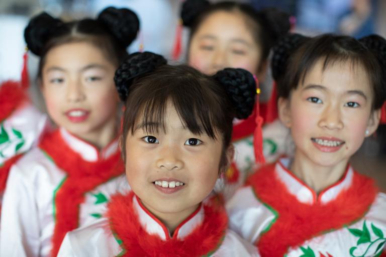 Quatre filles souriantes portant des vêtements assortis en blanc, rouge et vert. Partially obscured.
