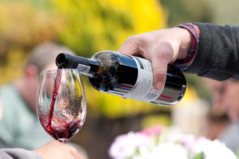 Red wine is poured from a bottle into a glass. Partially obscured.