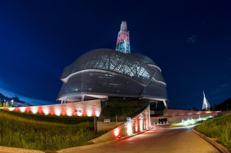 A building adorned with projected red-and-white stripes, topped by a glowing red tower. Partially obscured.