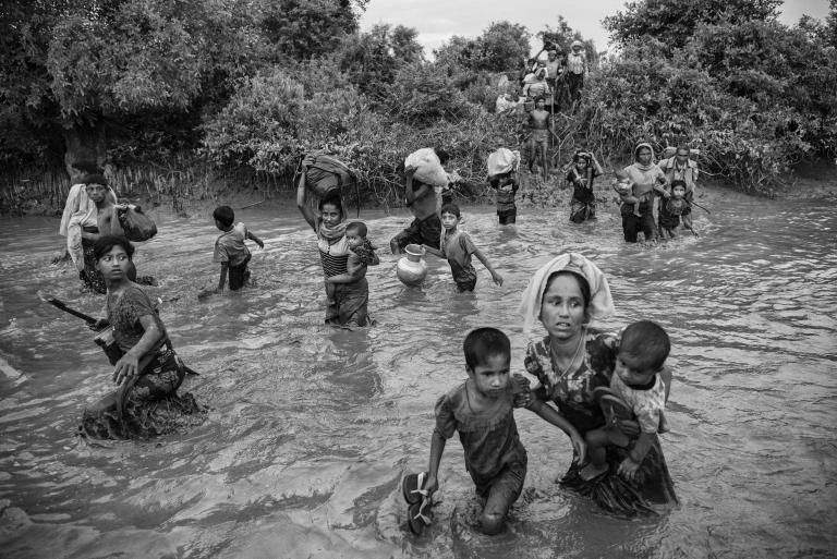 A group of Rohingya women and children carry their belongings as they wade across a canal filled with two to three feet of water.