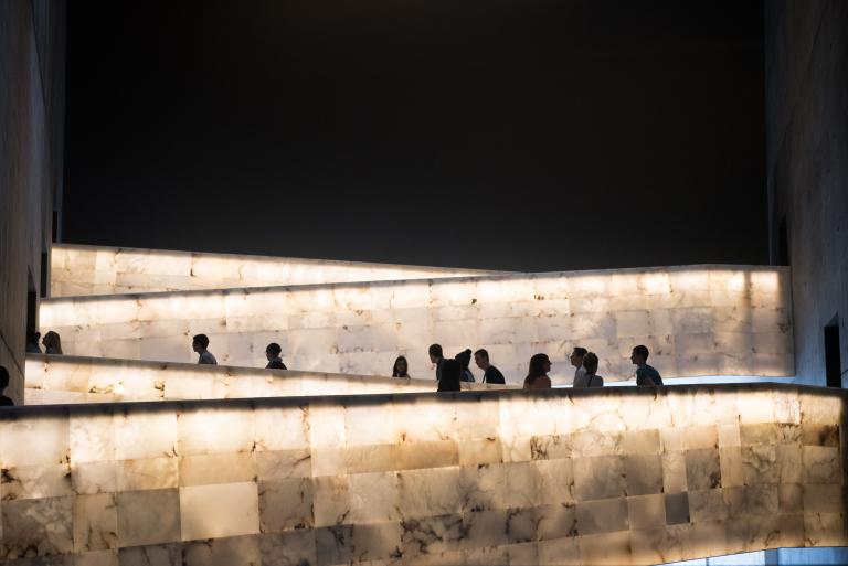 A group of people traveling up the Museum’s lighted alabaster ramps. Partially obscured.