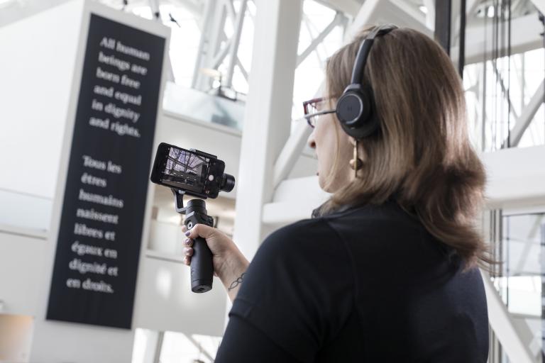 A woman holds a bar with a mobile phone attached to it and uses the screen to look at something off camera. Partially obscured.