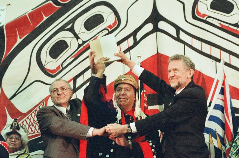 Three men clasp hands together while also holding a document above their heads.