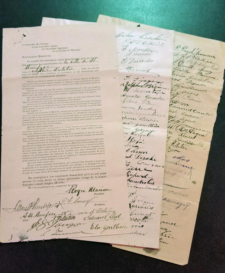 A close-up of an original French-language petition with two pages of signatures fanned out behind it.