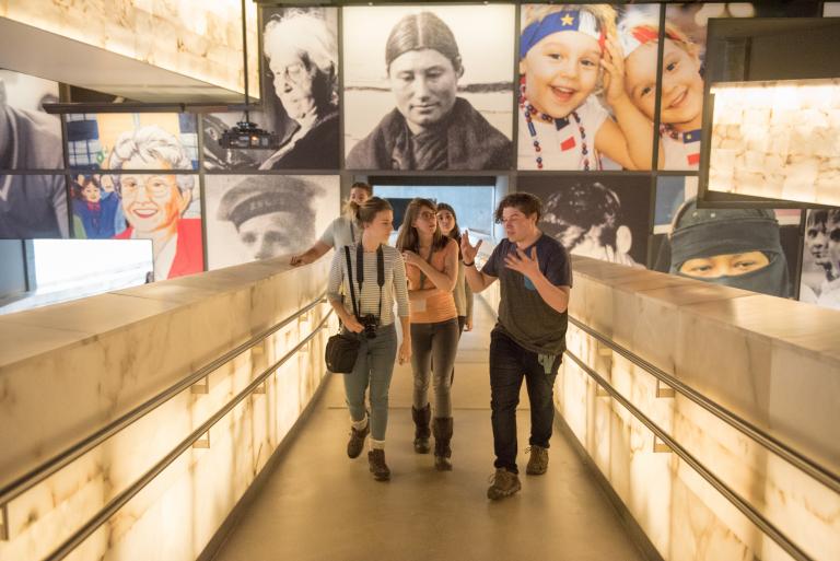 A group of young adults talk excitedly while walking up a set of illuminated ramps. Partially obscured.