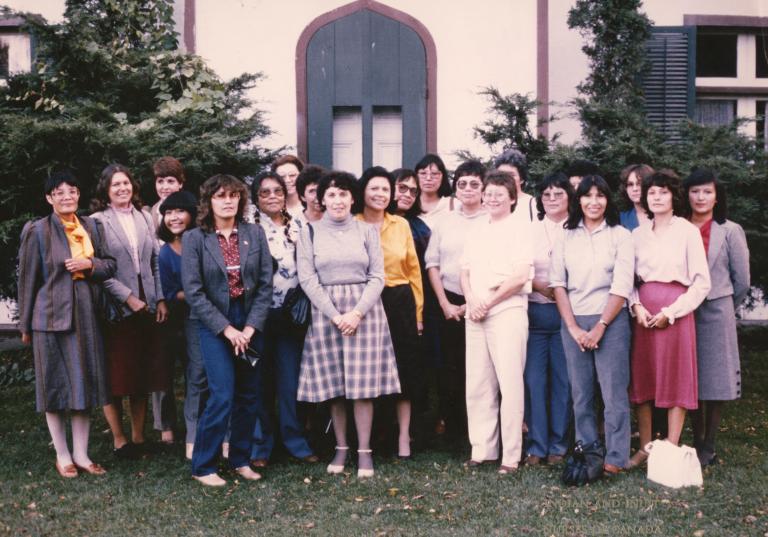 A group of Indigenous women nurses stand together outside. Partially obscured.