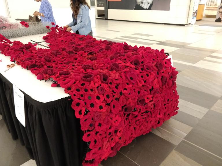 Two people are working at a table full of poppies. Partially obscured.