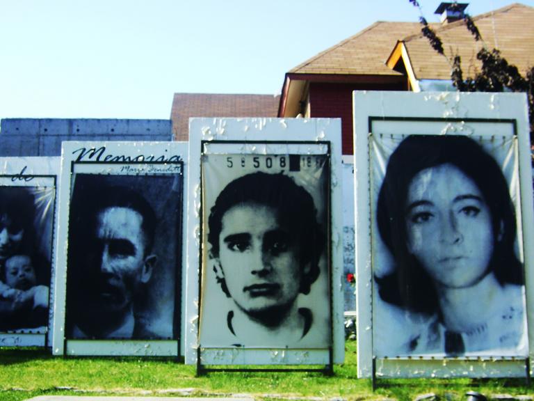 Outdoor display of large photographs of people’s faces. Partially obscured.