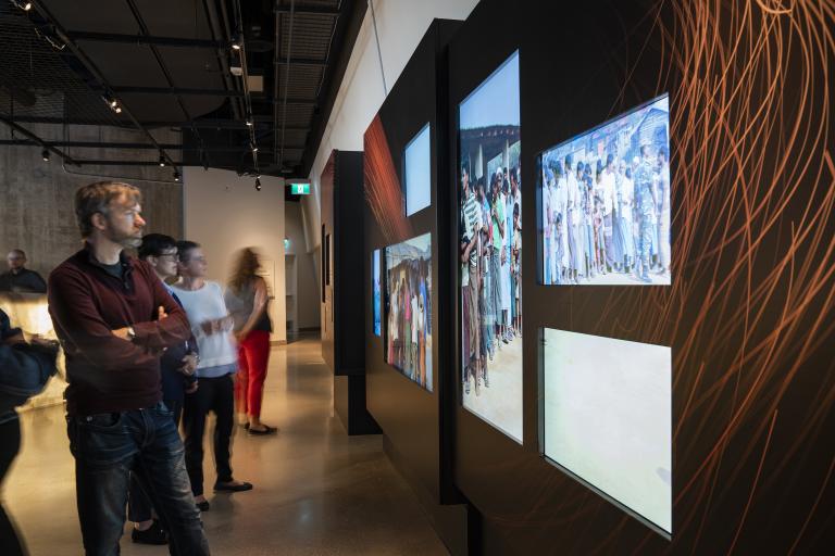 Several people looking at a display of colour digital photographs in a museum.