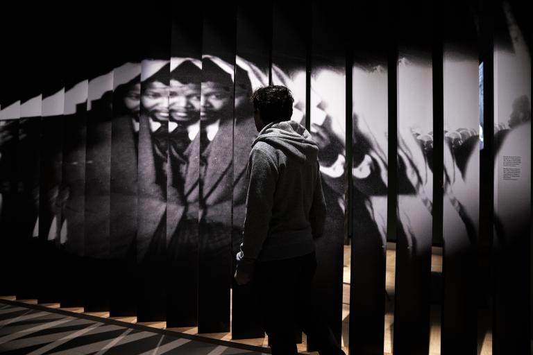 A person walks in front of a large photograph of Nelson Mandela. Partially obscured.
