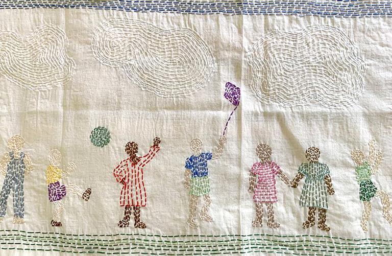 A piece of stitched fabric portraying families in diverse cultural clothing engaged in happy activities. Partially obscured.