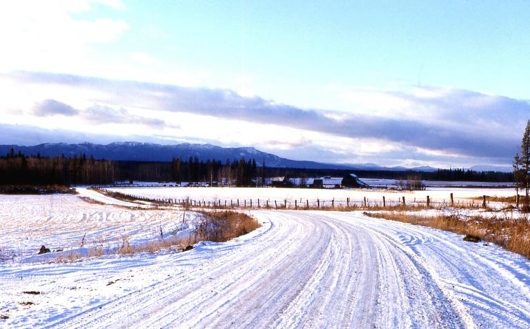 A snow-covered country road with mountains in the background. Partially obscured.