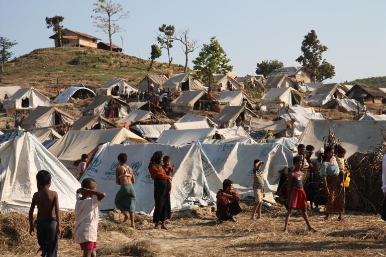 A densely packed camp of canvas tents on a hillside. Many people are visible inside and outside the tents.