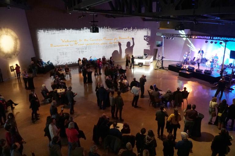 A crowd of people watches a band play on a brightly lit stage. Partially obscured.