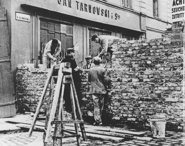 A group of men building a stone wall across a city street Partially obscured.