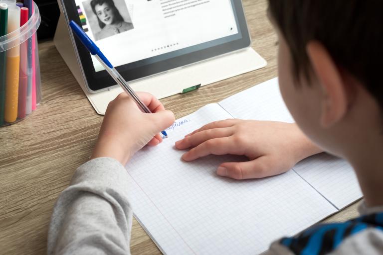 A youth studying at home with a tablet and doing school homework. Partially obscured.