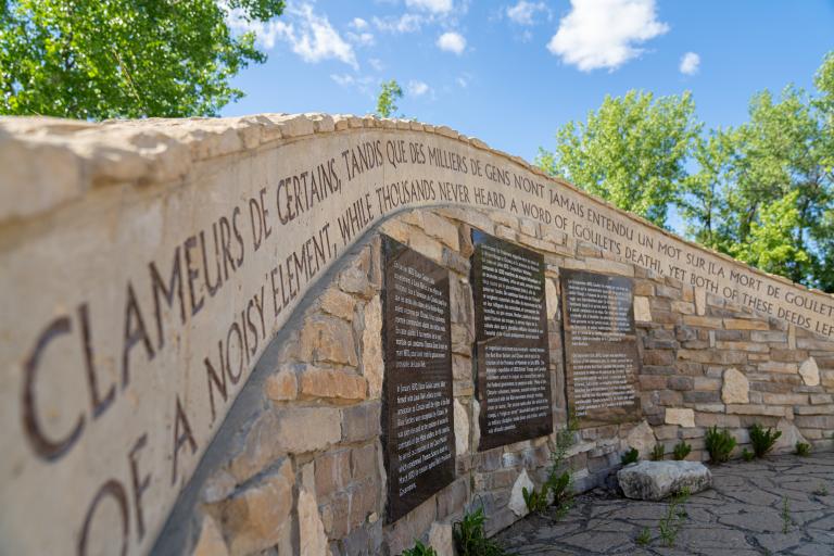 Rock and masonry sculpture shaped like a curved wall, displaying carved decorative text and informational panels.