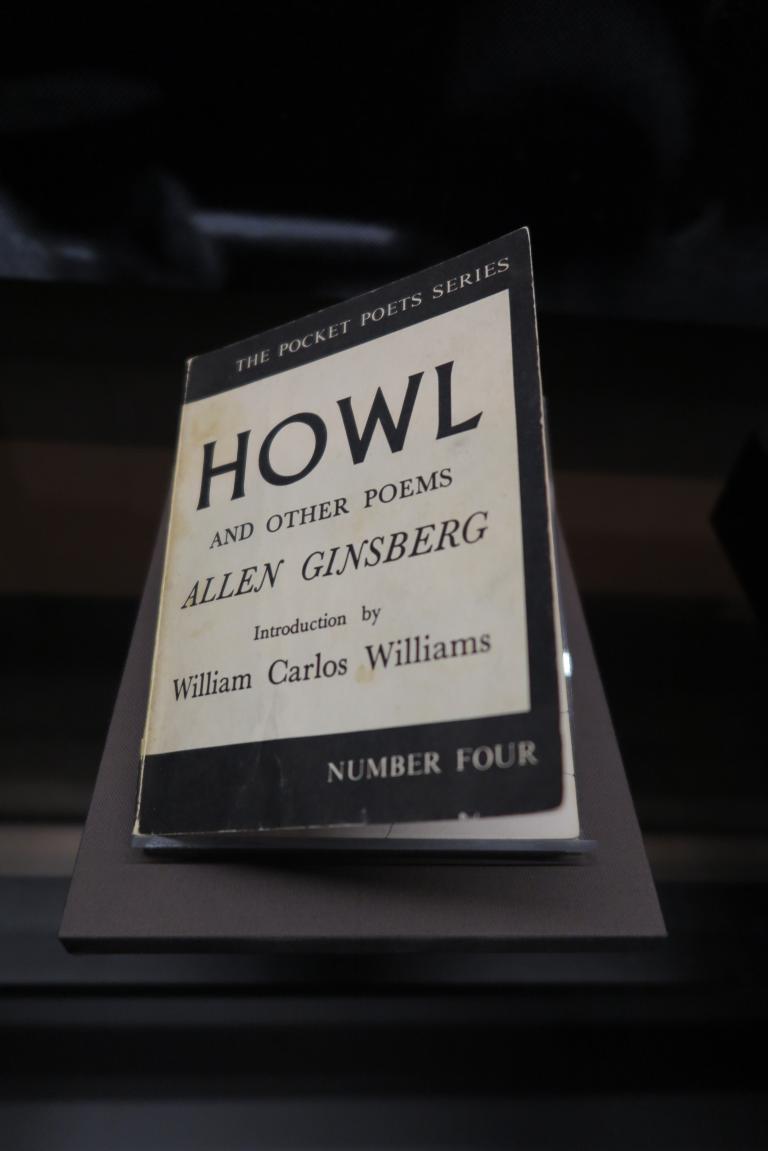A book on display. The cover reads: The Pocket Poets Series. Howl and Other Poems. Allen Ginsberg. Introduction by William Carlos Williams. Number Four. Partially obscured.
