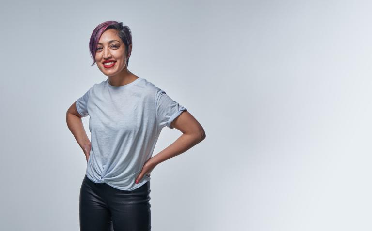A smiling woman with purple hair wearing a t-shirt. Partially obscured.