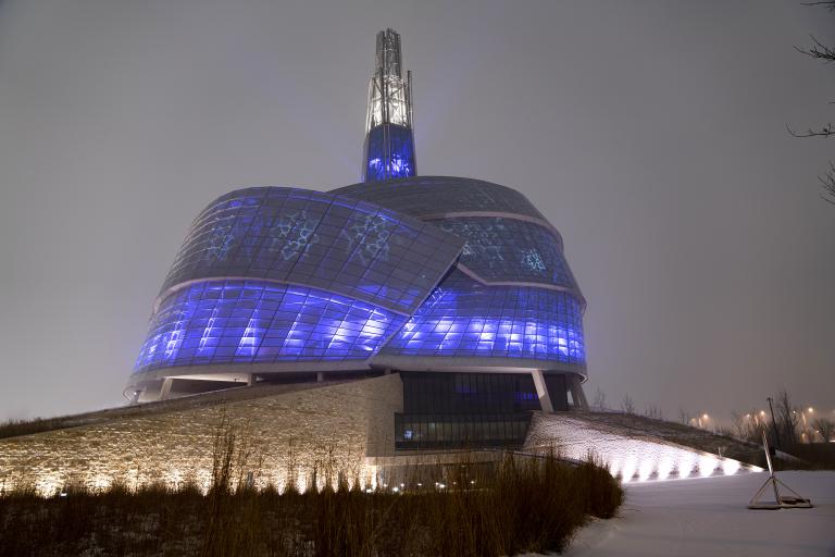 A building surrounded by glass panes illuminated in blue and purple. Snowflake designs are also projected on the windows. Partially obscured.