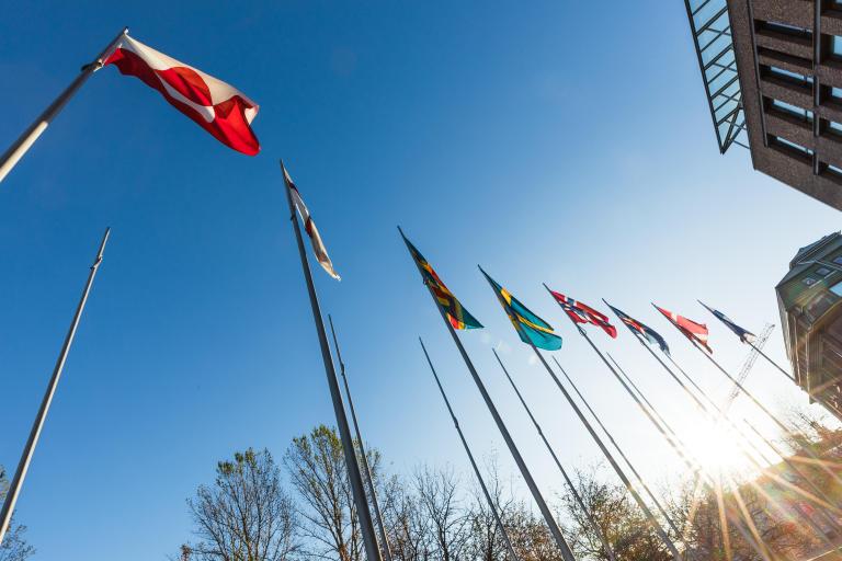 National flags fly side-by-side on tall flag poles. Partially obscured.