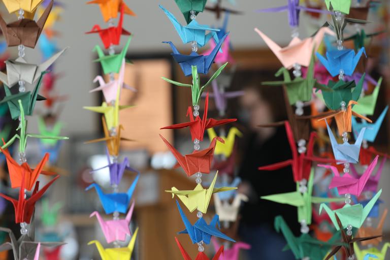 Colourful paper origami cranes hang in vertical rows. Partially obscured.
