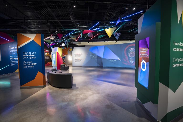 A museum gallery featuring artwork projected onto large screens and colourful geometric shapes. Partially obscured.