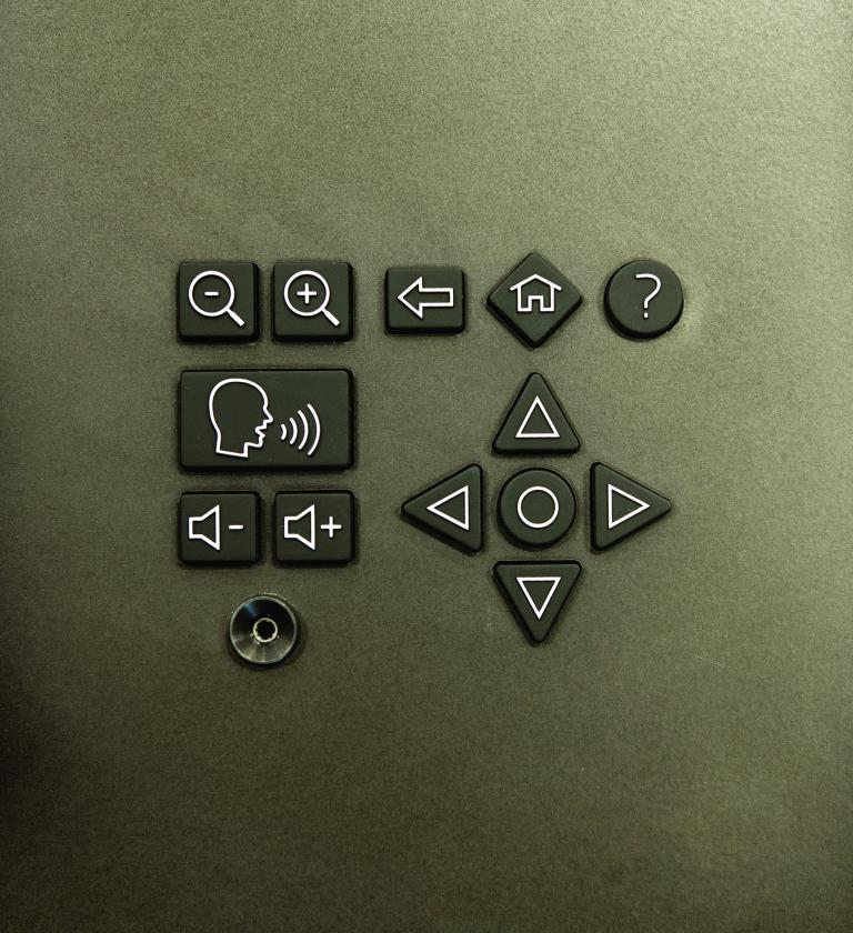 A headphone-style jack and a keypad with symbols indicating volume, magnification and navigation controls.