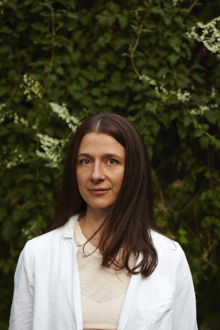 Headshot of a woman with long brown hair. She is wearing a white shirt.