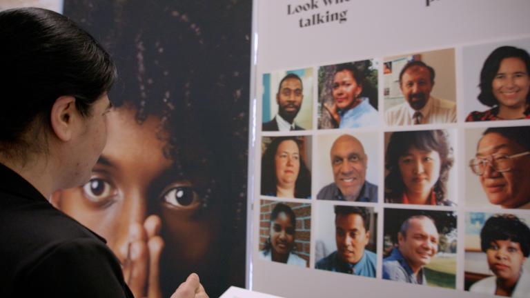 A woman gazes at a display showing faces of a diverse group of people. Partially obscured.