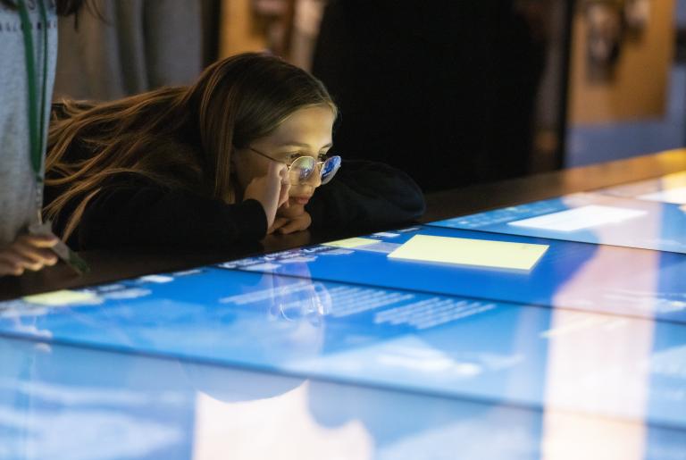 A girl looks at a horizontal interactive display with interest. Partially obscured.