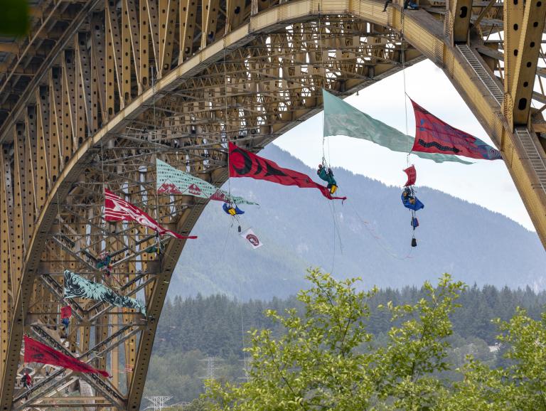 Several large triangular banners hang from the bottom of a large bridge.
