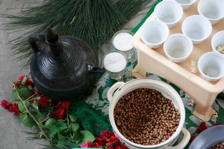 Close-up of someone pouring coffee from a Jebena, a traditional Ethiopian coffee pot. Partially obscured.