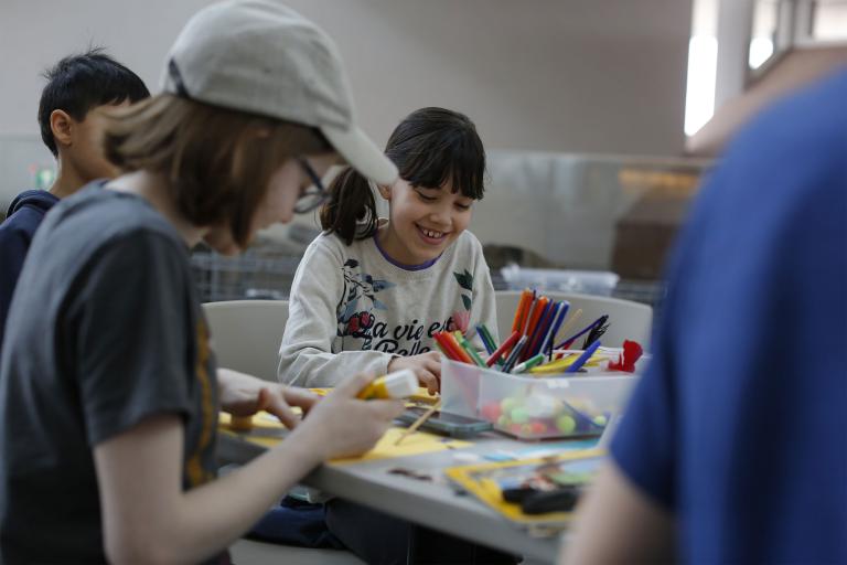 Children of different ages are sitting around a table doing crafts. Partially obscured.