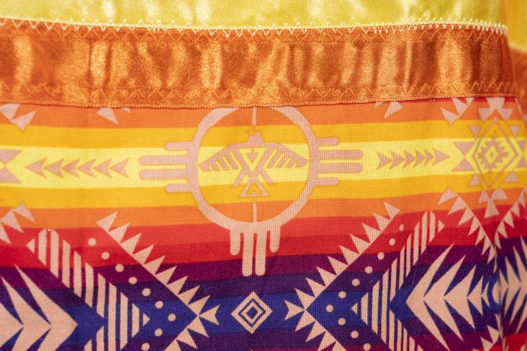 This section of the orange jingle dress shows a thunderbird. Partially obscured.