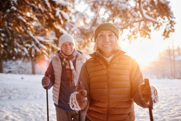 An older couple is walking through a wooded area using nordic poles. Partially obscured.