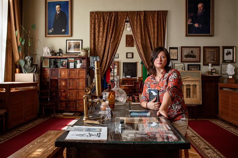A woman kneels beside a coffee table surrounded by books and heirlooms. Partially obscured.