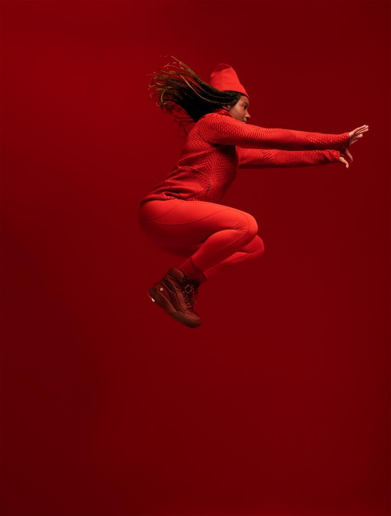 A black woman jumps in the air wearing an all red Olympic uniform. Partially obscured.