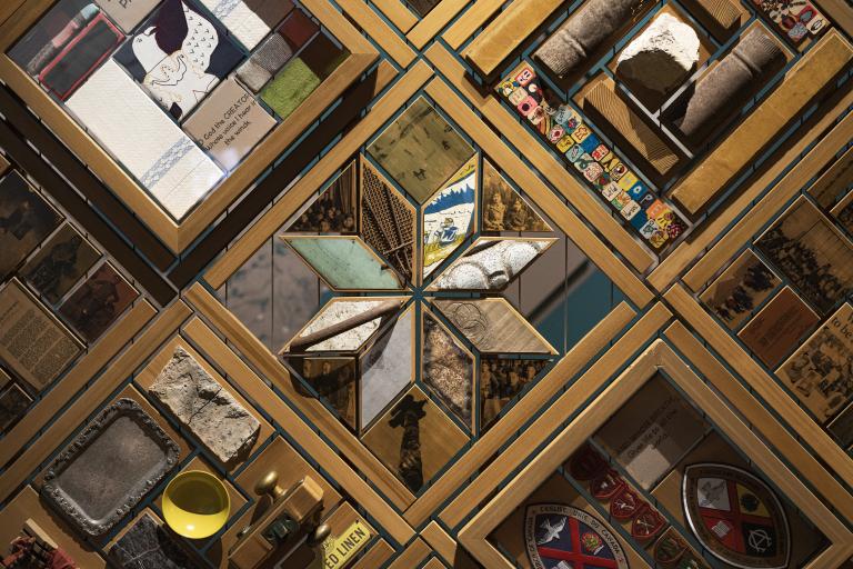 Many pieces of wood and other materials arranged in interlocking and repeating geometric patterns. Partially obscured.