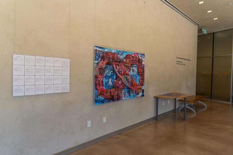 A mosaic of 24 tiles hangs on a wall next to a text panel. It depicts personal stories of Métis experiences in colonial schooling systems. Together the images show a red sash-inspired infinity symbol on a blue background.