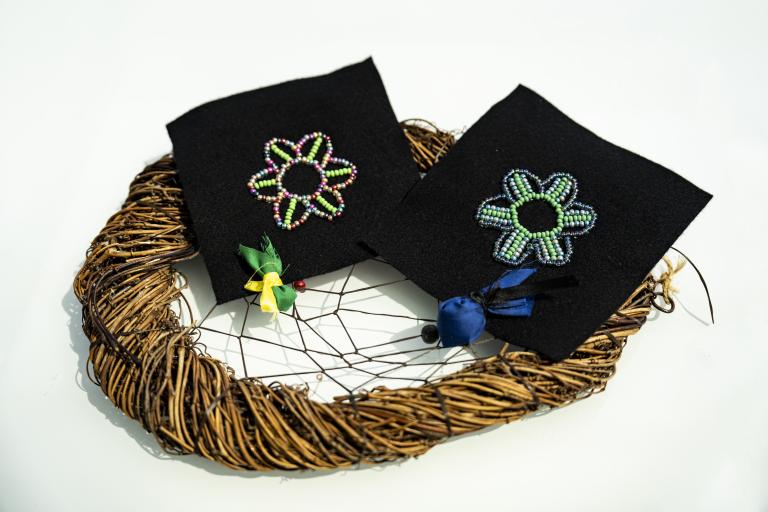 Two outline beading flowers with two tobacco ties on a dream catcher. Partially obscured.