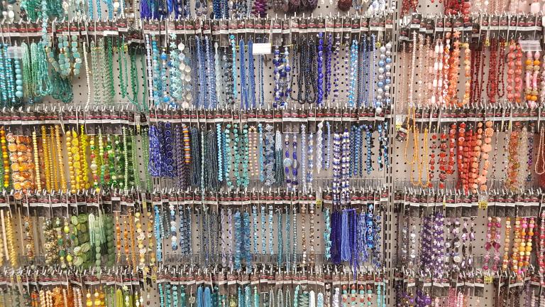 Brightly coloured beads in various shapes and sizes hang from hooks on a white pegboard. Partially obscured.