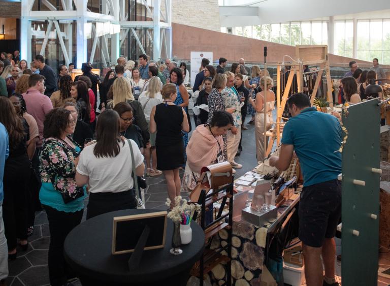A group of people gathering and chatting in a large hall. One person is shopping at a kiosk. Partially obscured.