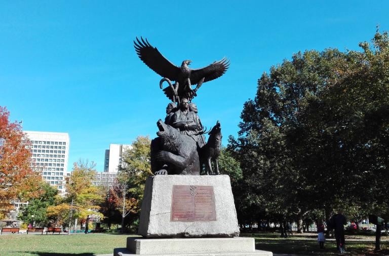 The National Aboriginal Veterans monument, an outdoor statue featuring three Indigenous veterans, a bear, a wolf and an eagle taking flight on top. Partially obscured.