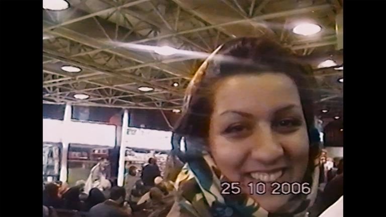 A smiling young woman in a headscarf stands in a crowd. The image has a date-stamp: 25-10-2006. Partially obscured.