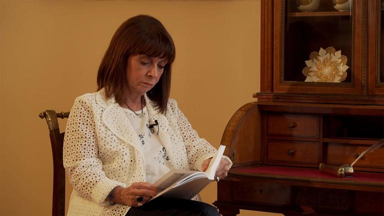 A woman sits reading a book. The woman is Katerina Sakellaropoulou, President of the Hellenic Republic. Partially obscured.